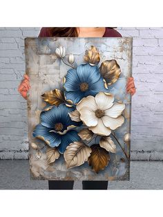 a woman holding up a painting with blue flowers on the front and gold leaves on the back