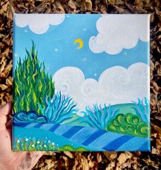 someone is holding up a painting on the ground with leaves in front of them and a blue sky