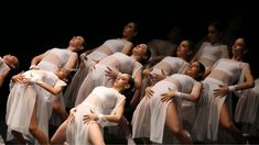 a group of dancers in white outfits with their arms around each other and one woman holding her head