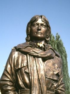 a bronze statue of a man wearing a jacket and scarf with trees in the background