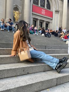 two people sitting on the steps in front of a building with many people standing around