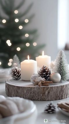 two lit candles sitting on top of a wooden slice with pine cones and ornaments around it