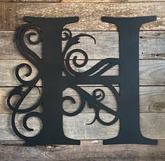 the letter h is made out of metal and sits on a wooden surface with wood planks