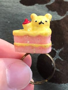 someone is holding a ring with a piece of cake on it that looks like a bear