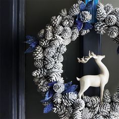 a white deer figurine sitting in front of a wreath with pine cones on it