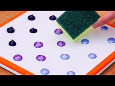 someone is using a sponge to clean the surface of a board with blue and purple dots