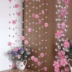 pink flowers are hanging from the curtain in front of a vase with purple flowers on it