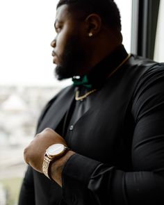 a man wearing a black shirt and green bow tie standing in front of a window