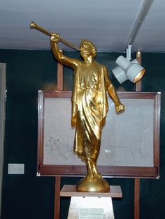 a gold statue holding a baseball bat on top of a wooden stand in front of a chalkboard