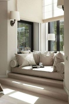 a window seat in the corner of a living room with pillows and blankets on it