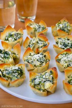 small appetizers with spinach and cheese are on a white plate next to two glasses