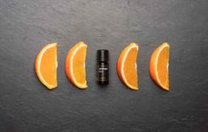 three oranges and one roll - on perfume bottle sitting in the middle of five slices