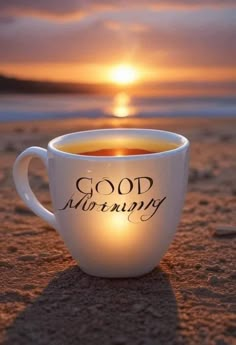 a coffee cup with the words good morning on it sitting in the sand at sunset