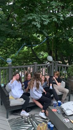 a group of women sitting on top of a wooden bench next to each other in front of trees