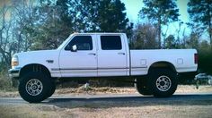 a white truck parked on the side of a road next to some grass and trees