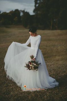 a woman in a white dress holding a bouquet and wearing a long sleeved wedding dress