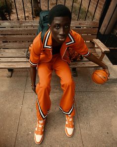 a man sitting on a bench with a basketball in his hand and wearing an orange uniform