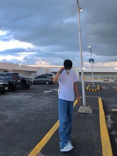 a man standing in the middle of a parking lot talking on his cell phone while wearing a white t - shirt and blue jeans