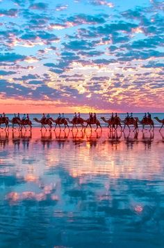 a group of people riding on the backs of camels across a body of water