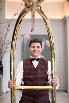 a man in a vest and bow tie holding up a gold frame