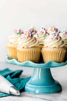 cupcakes with white frosting and sprinkles on a blue cake plate