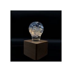 a clear glass light bulb sitting on top of a wooden block in front of a black background