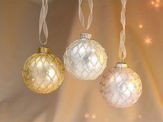 three glass ornaments hanging from strings on a string with lights in the background and snowflakes