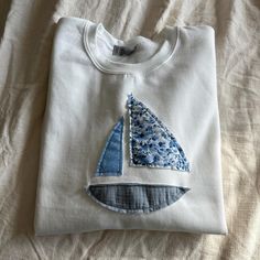 a white t - shirt with a blue sailboat appliqued on it