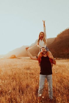 a man carrying a woman on his shoulders in the middle of an open field at sunset