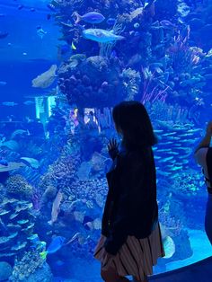 two people standing in front of an aquarium looking at the fish and corals inside