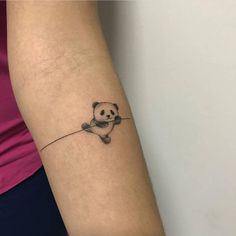 a small panda bear tattoo on the left inner arm and wrist, with a tiny line drawing of a teddy bear holding a string