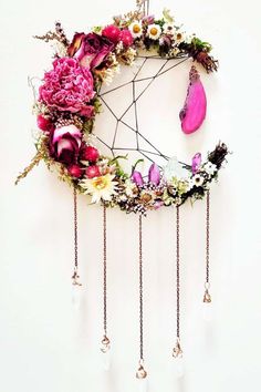 a pink flowered dream catcher hanging on the wall next to a white wall with beads and flowers