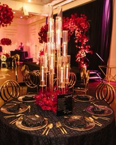 a black table topped with lots of plates covered in red flowers and vases filled with candles