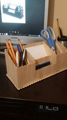 a desk with a computer monitor, pen and pencils in a cardboard box on it