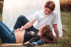 a pregnant woman laying on the ground next to a man who is holding her belly