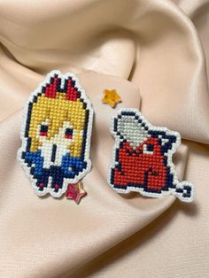 two cross stitch patches sitting next to each other on a white cloth covered tablecloth