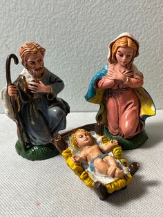 two nativity figurines, one holding a baby jesus and the other sitting down