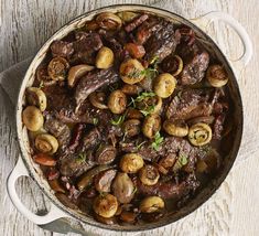 a pot filled with meat and mushrooms on top of a wooden table