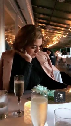 a woman sitting at a table in front of a glass of wine and some drinks