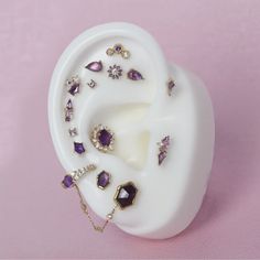 a white earring with purple and gold jewelry on it's side, against a pink background