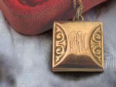 "Description: Lovely antique fob locket in a square shape that features a different monogram on both sides. The center where the monograms are engraved is also slightly bowed giving this fob locket a bit more depth.  The initials of what appears to be MSL and CRM in an old cursive font are engraved on this antique form locket.  The locket hangs as a square pendant. The antique pendant is gold filled, and is circa late 1800s to early 1900s in age.  On either side of the monograms is a repousse sc Antique Locket, Cursive Font, Antique Pendant, Older Fashion, Scroll Design, Square Pendant, Early 1900s, Locket Necklace, Gold Filled Chain