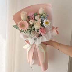 a bouquet of flowers is being held by a woman's hand in front of a window