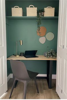 a laptop computer sitting on top of a wooden desk in front of a green wall