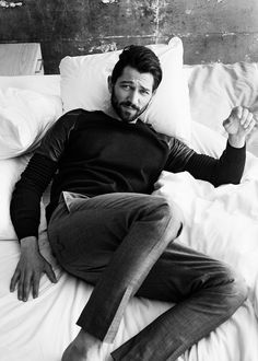 a man laying on top of a bed in a black and white photo next to pillows