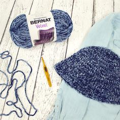 yarn, crochet hook and knitting needles laid out on a white wooden surface