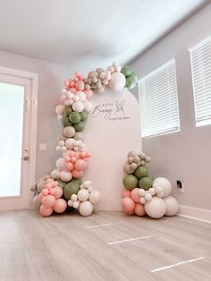 an arch made out of balloons in the middle of a room with white walls and wooden floors