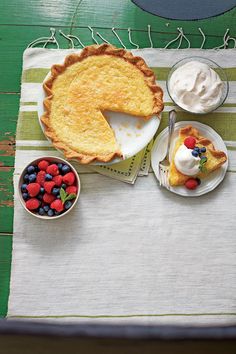 a table topped with pies and fruit on top of plates next to bowls of whipped cream