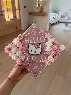 a person holding up a pink graduation cap with hello kitty on it and flowers in the middle