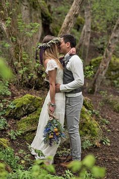 a bride and groom kissing in the woods with greenery around them on their wedding day