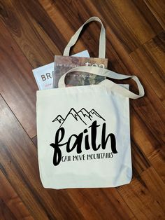 a tote bag with the words faith can move mountains on it sitting on a wooden floor